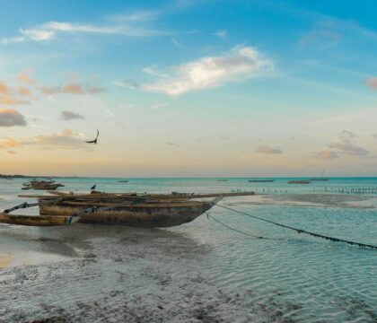 Idyllic Zanzibar beach in Tanzania, featuring calm turquoise waters lapping at white sands, with traditional wooden boats anchored near the shore under a vibrant blue sky dotted with fluffy clouds.