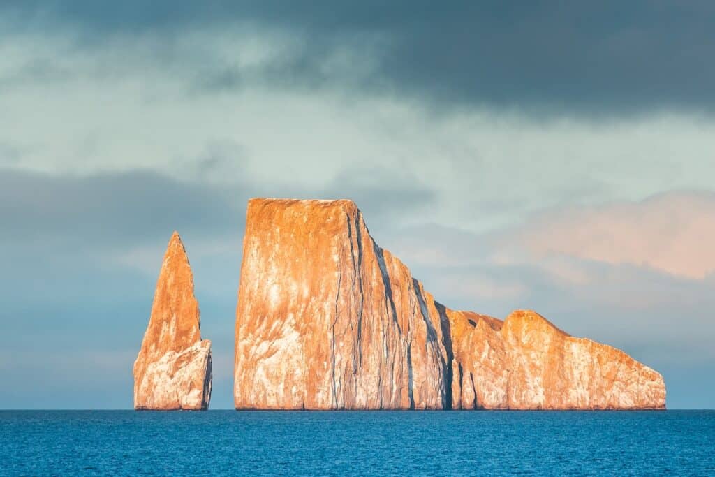 A scenic view of Kicker Rock in the Galápagos, rising dramatically from the ocean under a clear sky, with calm waters in the foreground.