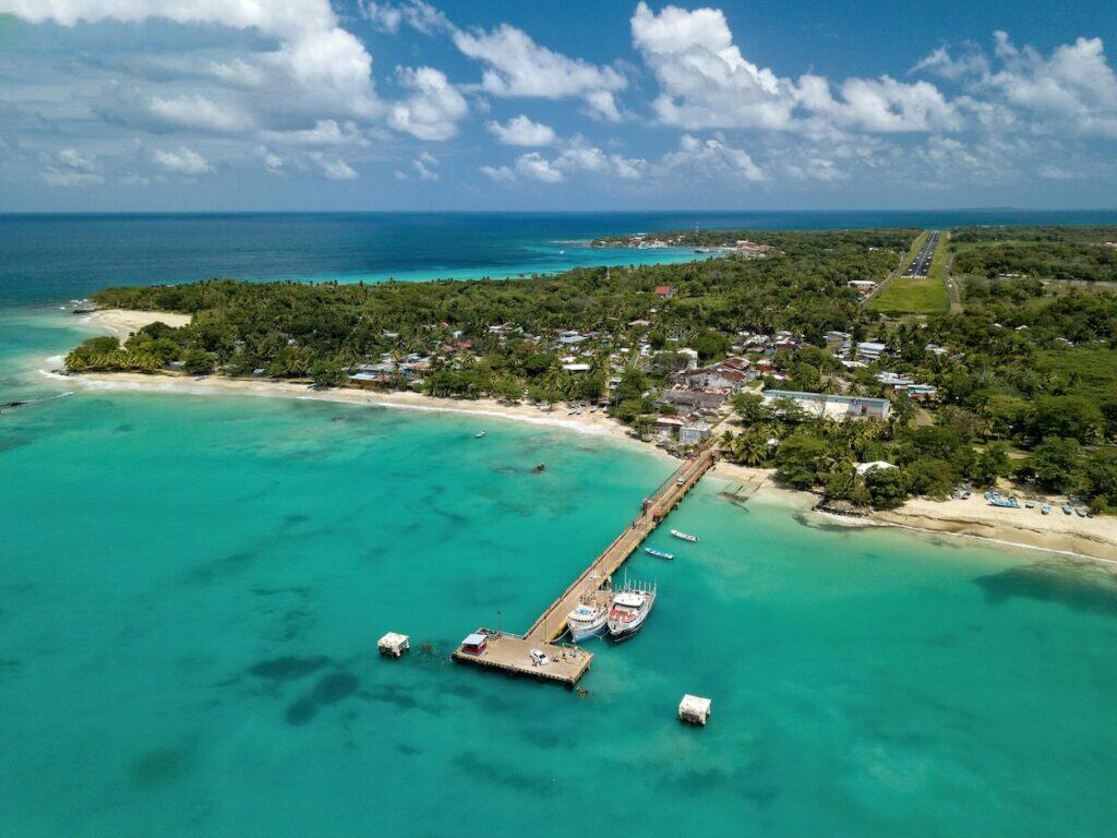 Aerial view of the turquoise coastline and dock on Little Corn Island, Nicaragua, with boats moored along the pier and lush green jungle in the background.
